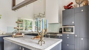 Et moderne køkken med en central ø, integrerede hårde hvidevarer og et stort vindue, der giver naturligt lys.