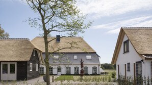 A traditional house with a thatched roof, white walls, and a small garden area with a tree and shrubs. - Bungalow on Texel Near De Slufter Reserve (De Cocksdorp)