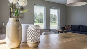 A modern living room with a wooden dining table, a vase with white flowers, and a white decorative basket. - Bungalow on Texel Near De Slufter Reserve (De Cocksdorp)
