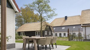 A patio with a table and chairs, a thatched-roof building, and a brick wall. - Bungalow on Texel Near De Slufter Reserve (De Cocksdorp)