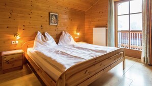 A wooden cabin bedroom with a bed, nightstands, a wall-mounted light, and a window with a view. - Cozy Chalet With Sauna in Grossarl (Grossarl)