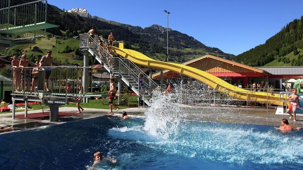 A swimming pool with a water slide, surrounded by a mountainous landscape. - Cozy Chalet With Sauna in Grossarl (Grossarl)