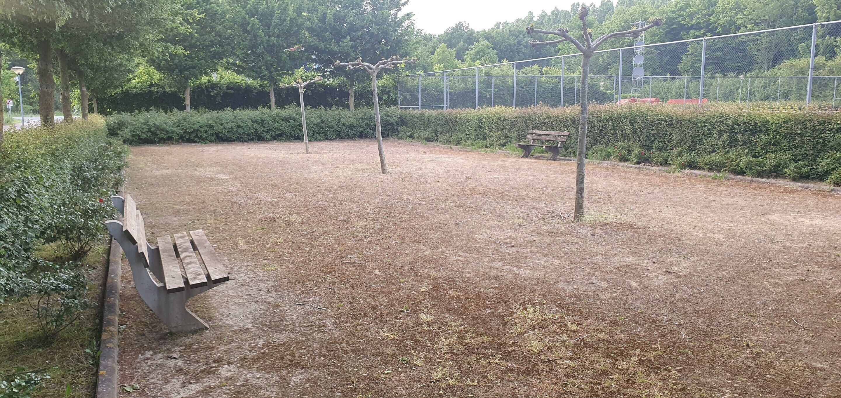 Un espace extérieur avec un sol en terre battue, un banc en bois et une clôture.