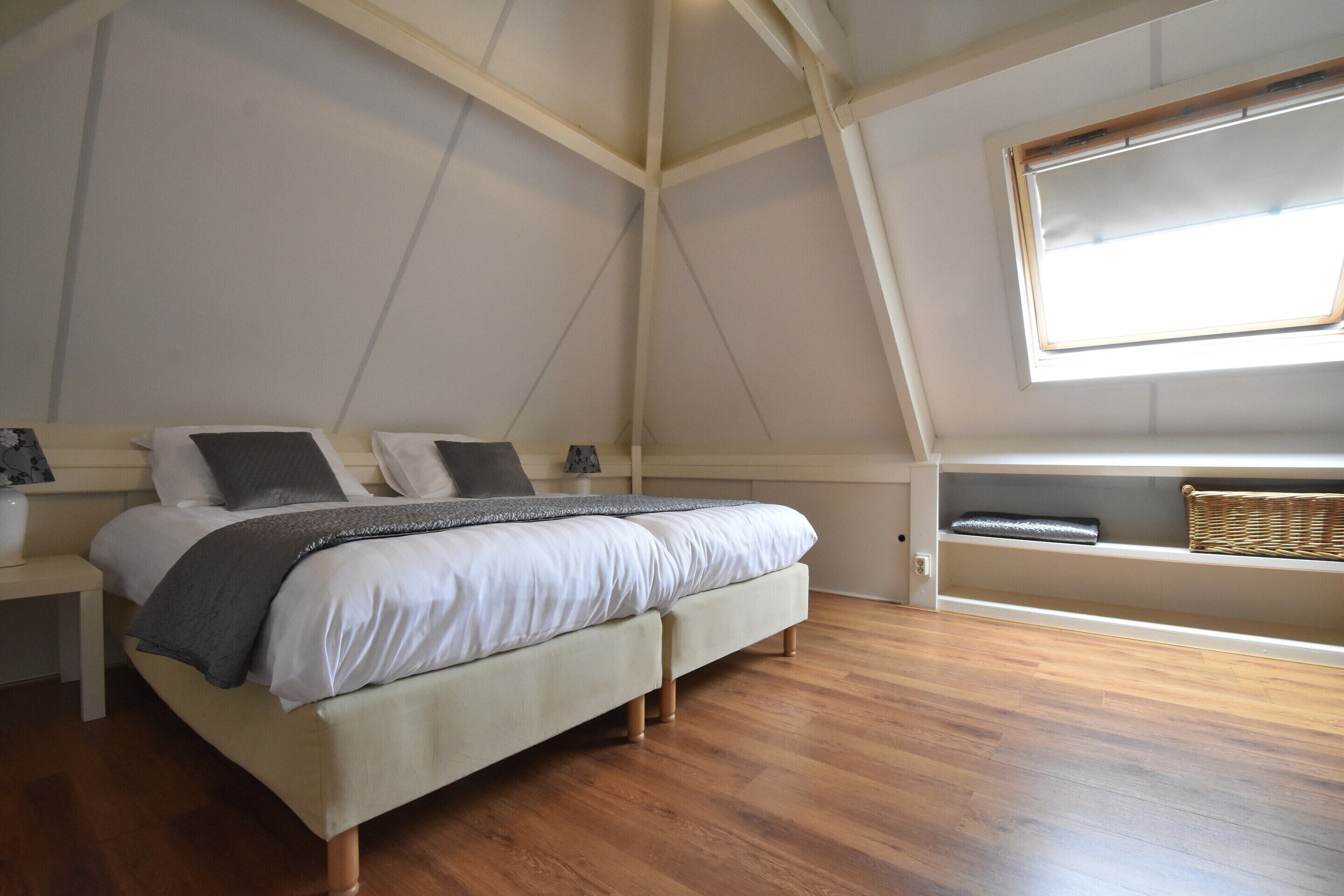 Quarto com cama, soalho de madeira, janela e prateleira com cesta.