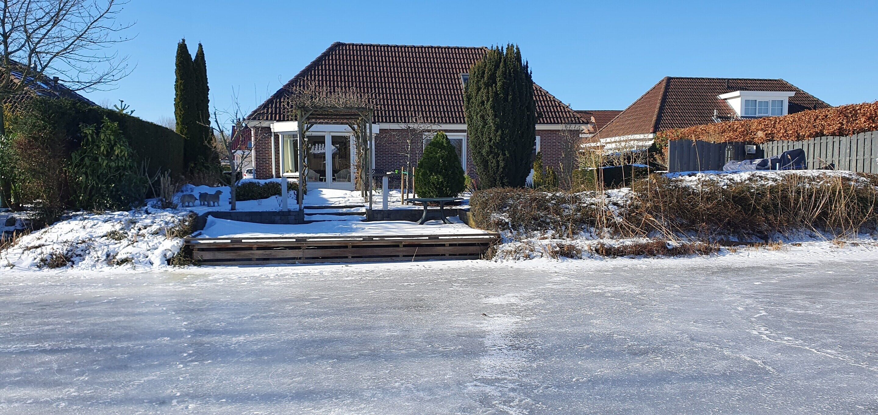 A residential area with a house featuring a tiled roof, a wooden deck, and a snow-covered driveway.