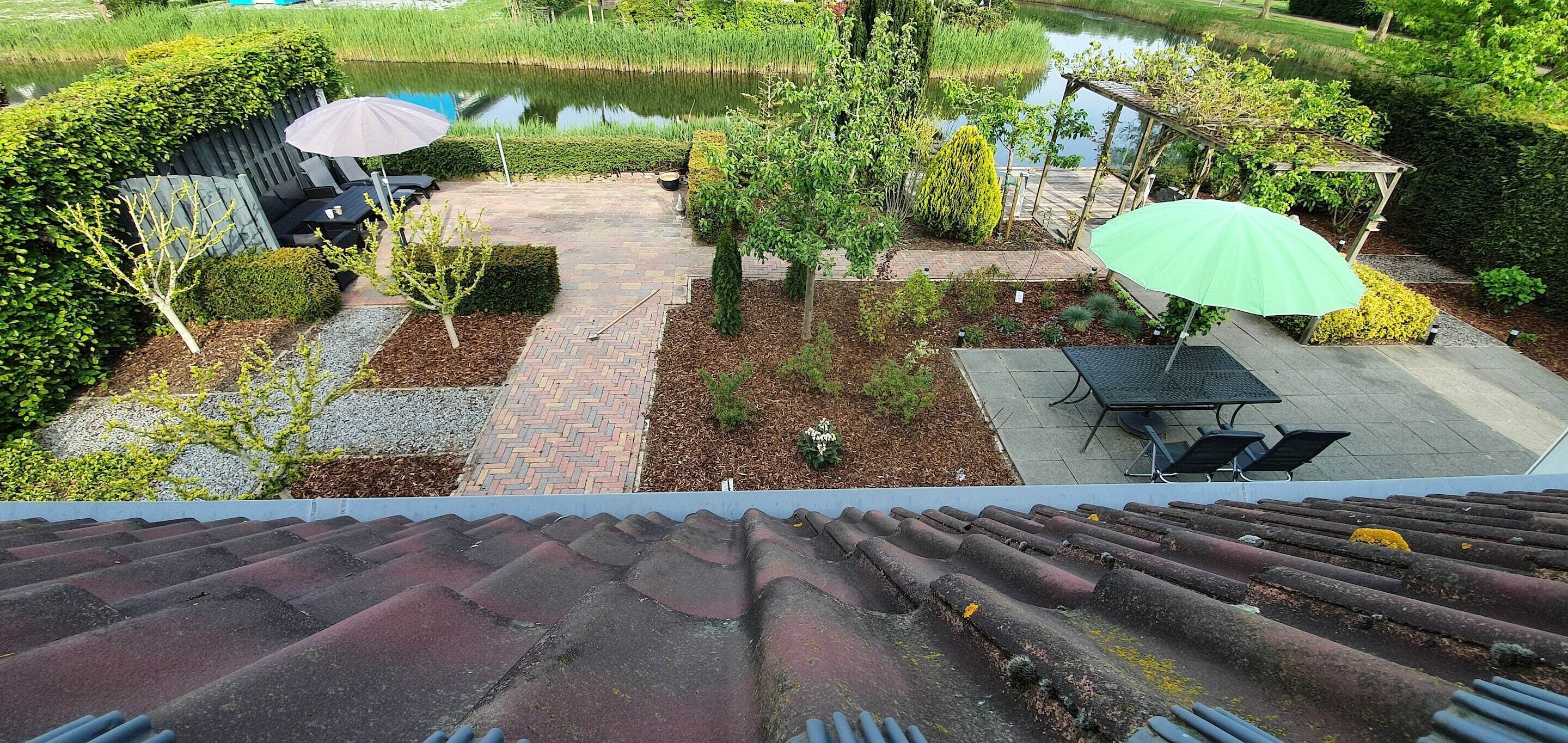 Una terraza en la azotea con vistas a un jardín, un estanque y una pérgola con un parasol verde.