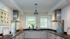 A modern kitchen with white cabinets, black countertops, and a central island. There are two windows providing natural light, and a hanging light fixture above. - Pet-friendly Mansion (Swolgen)