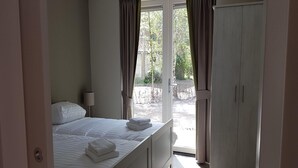 Un dormitorio con cama, mesita de noche, armario y ventana con cortinas.