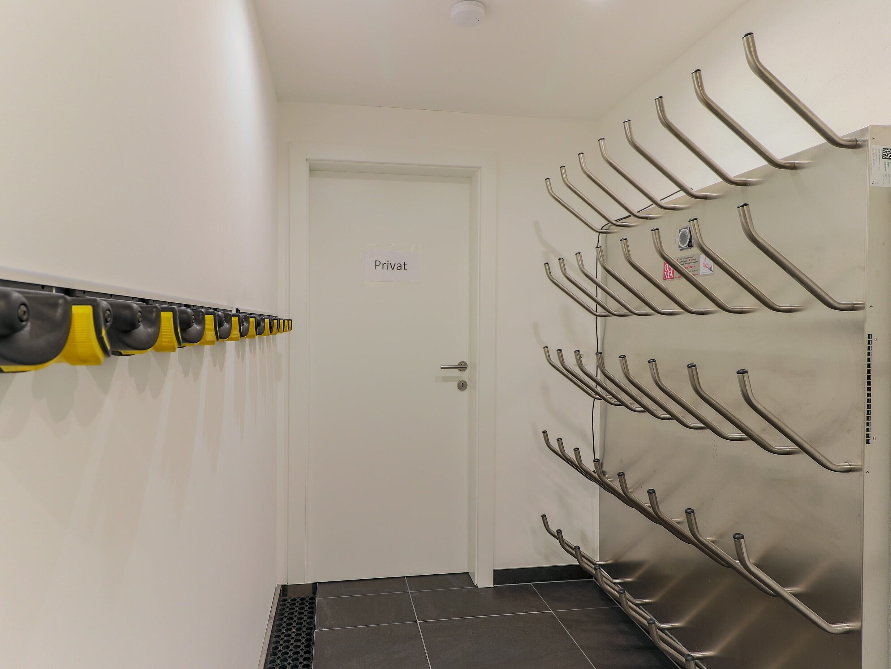 A hallway with a 'Privat' door, a coat rack with yellow and black items, and a metal rack with hooks.