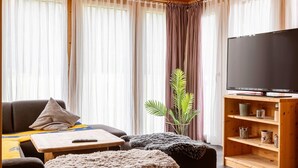 A cozy living room with a sofa, a coffee table, a TV on a wooden stand, and a plant. - Luxurious Chalet in Murau with Outside Hot Tub (Murau)
