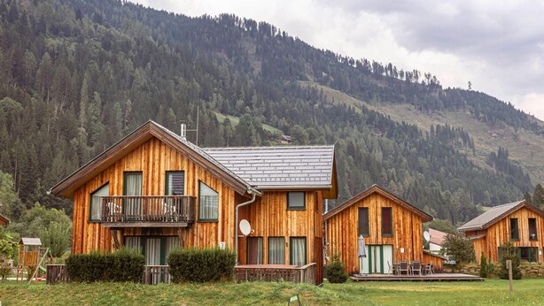 A wooden cabin with a balcony, surrounded by a grassy area and a forested mountain backdrop. - Luxurious Chalet in Murau with Outside Hot Tub (Murau)