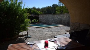 Eine Terrasse im Freien mit einer Steinwand, einem Holztisch, der zum Essen gedeckt ist, und einem Pool im Hintergrund.