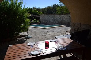 Eine Terrasse im Freien mit einer Steinwand, einem Holztisch, der zum Essen gedeckt ist, und einem Pool im Hintergrund.