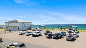 Ein Parkplatz mit mehreren Fahrzeugen, ein Gebäude mit dem Schild 'Tea Gardens Hawks Nest' und Blick auf das Meer.