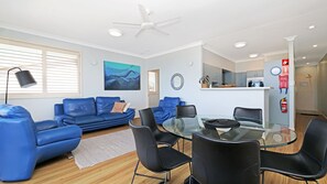 Una sala de estar moderna con una mesa de comedor de vidrio, sofás azules y un ventilador de techo.