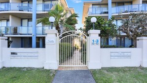 Ein Gebäude mit Balkonen und einem Palmbaum, das durch ein Tor zugänglich ist. Ein Schild weist auf die ‚Nautilus Holiday Apartments‘ hin, mit den Einheiten 1-3.