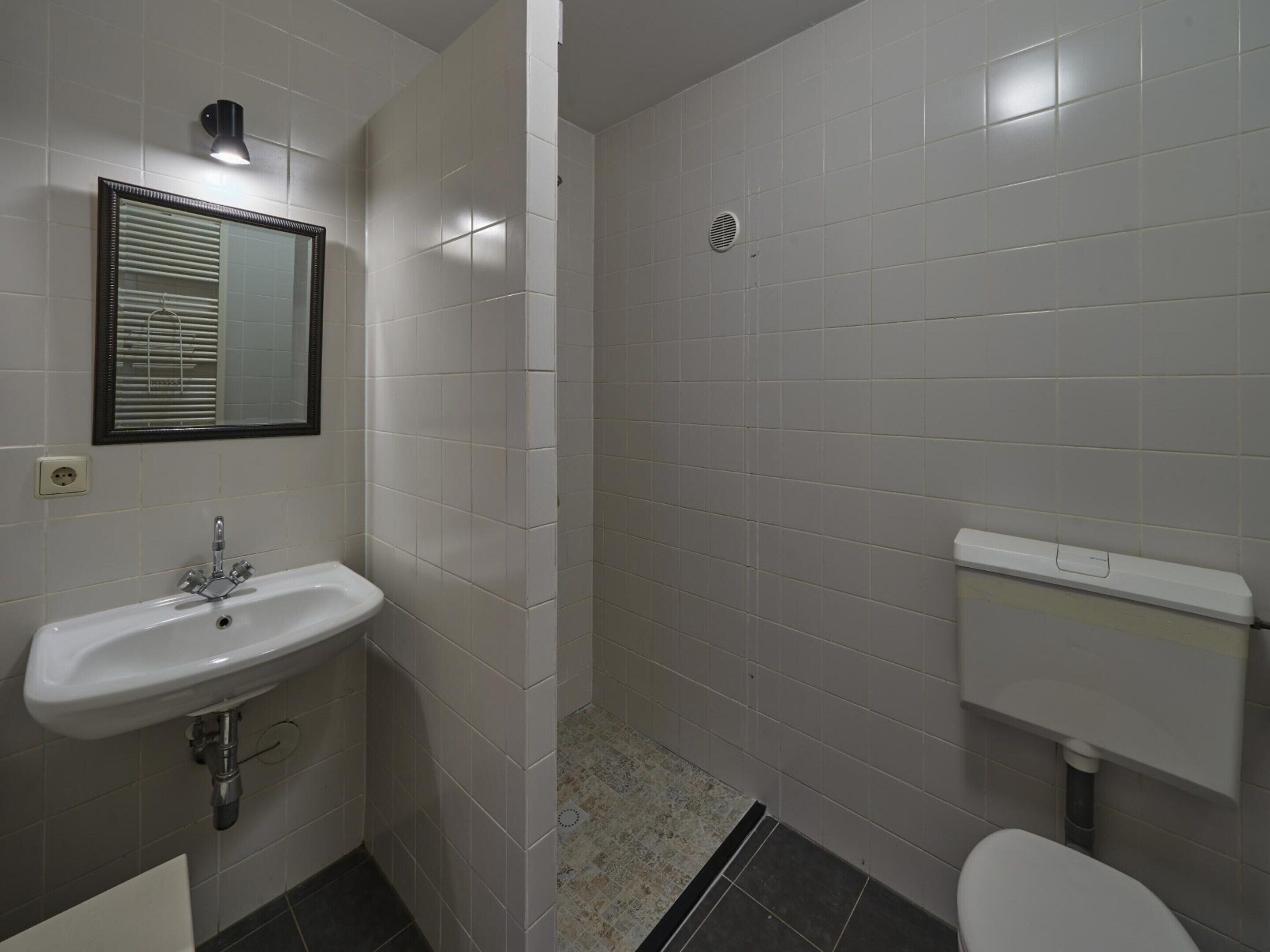 A bathroom with a white sink, mirror, toilet, and tiled walls.