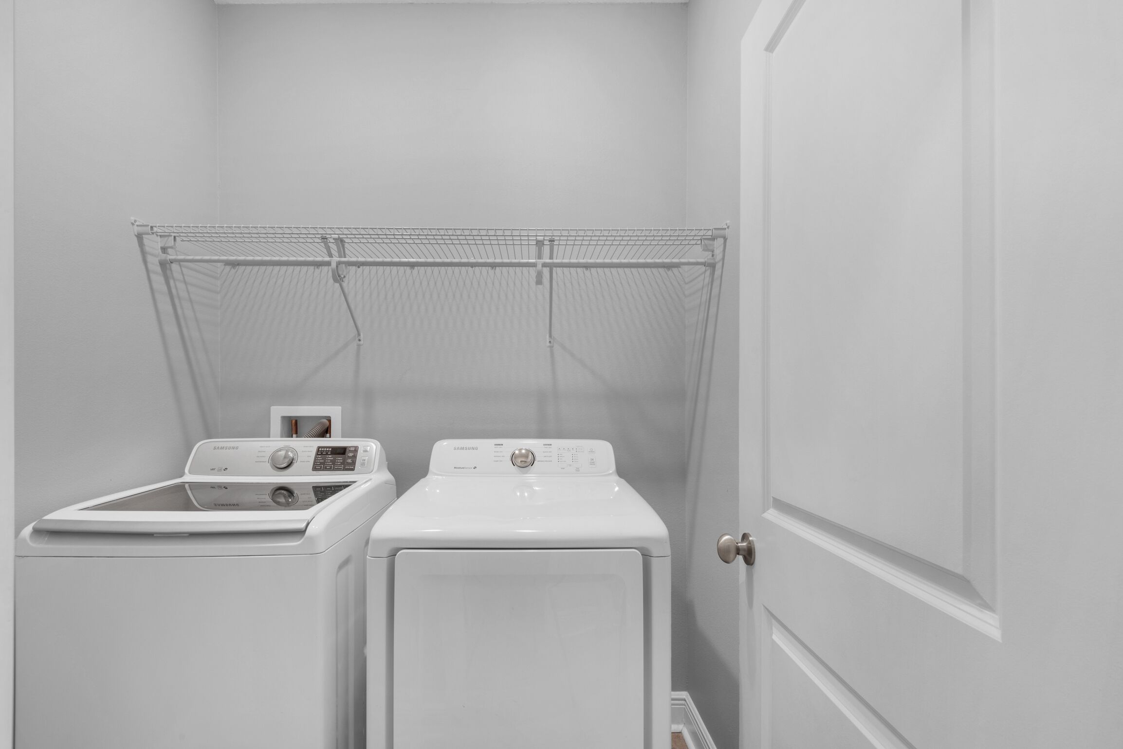 A laundry room with a front-loading washer and dryer, a drying rack, and a door.
