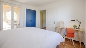 Ein Schlafzimmer mit einem großen Bett, einem Schreibtisch mit Stuhl, einem blauen Kleiderschrank und einer Tür, die auf einen Balkon führt.
