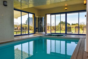 Una piscina interior con paredes de vidrio transparente, un jacuzzi y vistas al exterior.