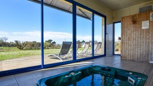 A hot tub in a room with large sliding glass doors leading to a patio with lounge chairs. - Seaside Villa With Pool in Moelan (Moelan-sur-Mer)