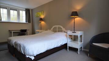 A bedroom with a large bed, two bedside tables with lamps, a chair, a desk, and a window with curtains.