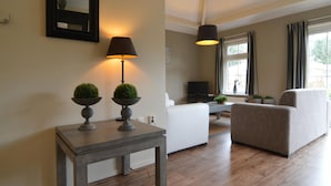 Un salon moderne avec un plancher en bois, un canapé blanc, un fauteuil gris et une petite table sur laquelle sont posées deux lampes.