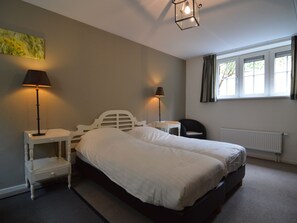 A bedroom with a large bed, two bedside tables, a chair, a radiator, and a window with curtains. - Holiday Home in the Veluwe in Nature (Putten)