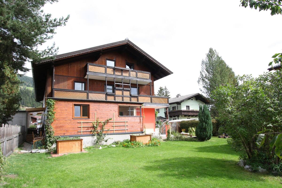 A modern multi-story house with a wooden facade, a balcony, and a well-maintained garden.