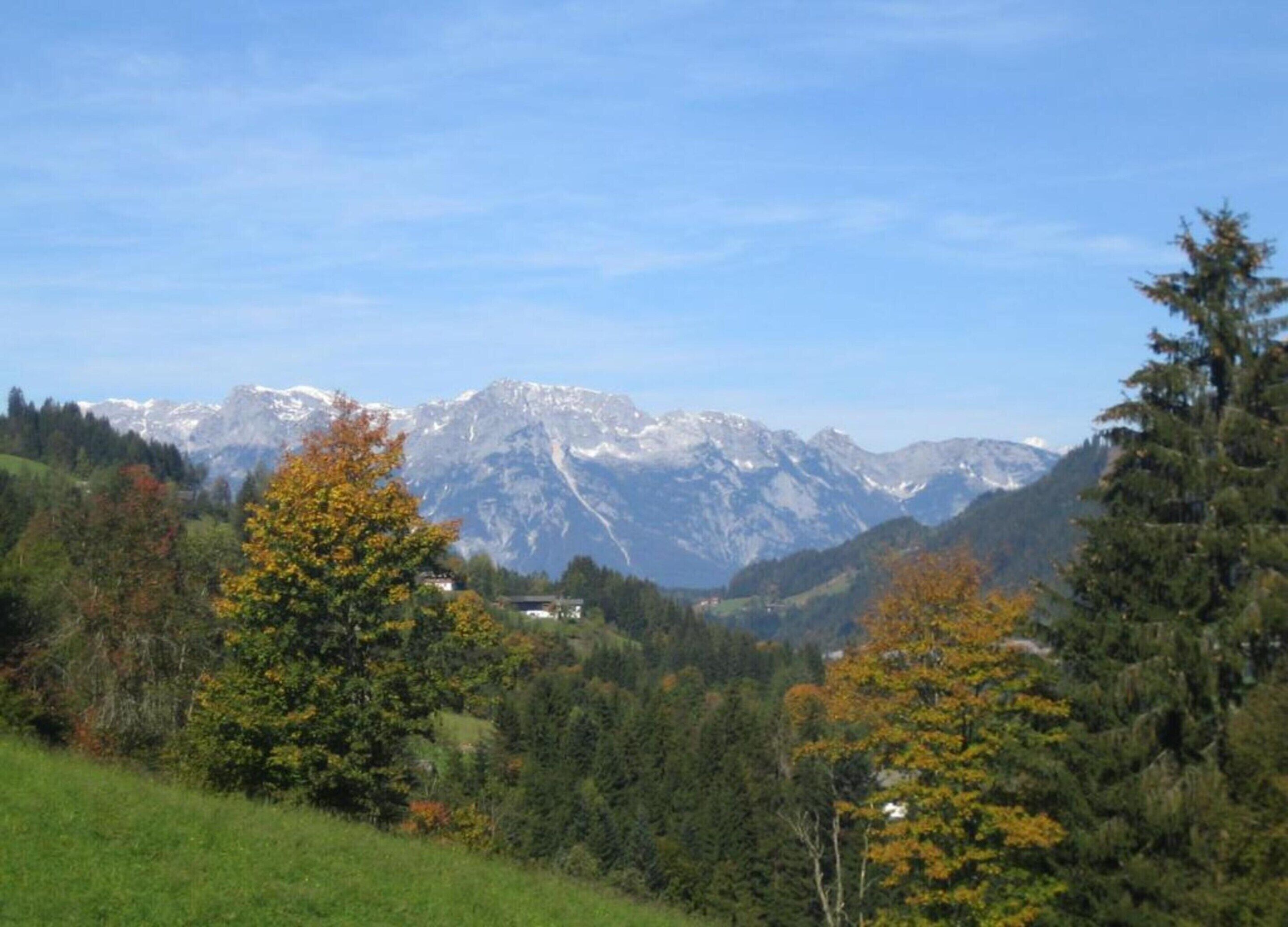 A mountain landscape with a house in the foreground and snow-capped peaks in the background.