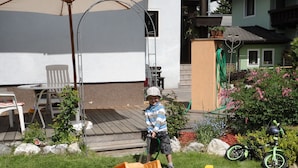 A child playing with a toy tractor and a wheelbarrow in a garden area with a patio table and chairs, a bicycle, and a house in the background. - Plush Apartment in Altenmarkt im Pongau near Ski Area (Altenmarkt im Pongau)