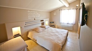 Een slaapkamer met een bed, nachtkastje, stoel, wandplank, raam met gordijnen en een citaat op de muur.