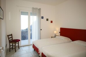 Une chambre d’hôtel avec deux lits, une chaise, une petite table et une fenêtre avec des rideaux.