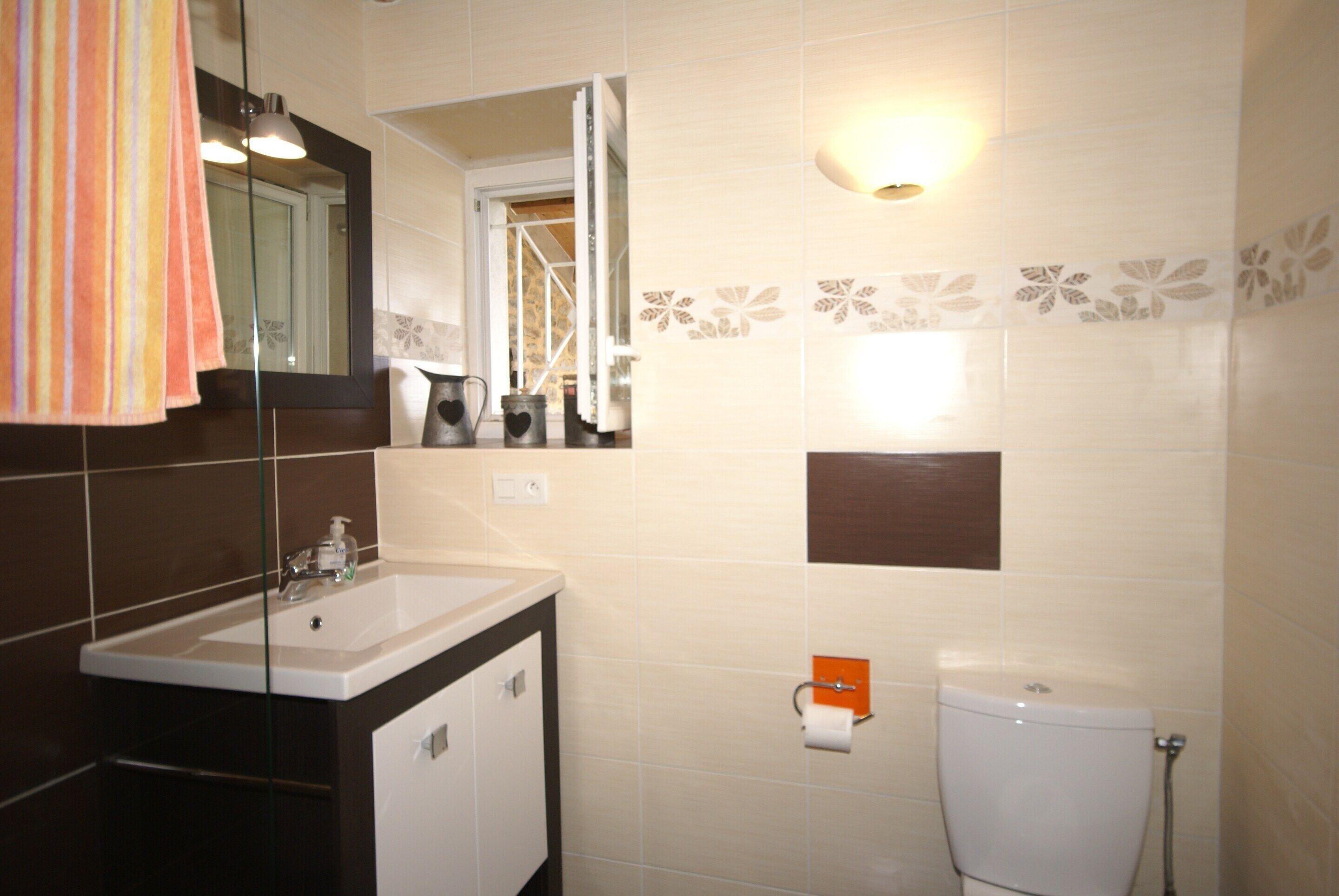 A bathroom with a sink, mirror, toilet, and a towel hanging on the wall.