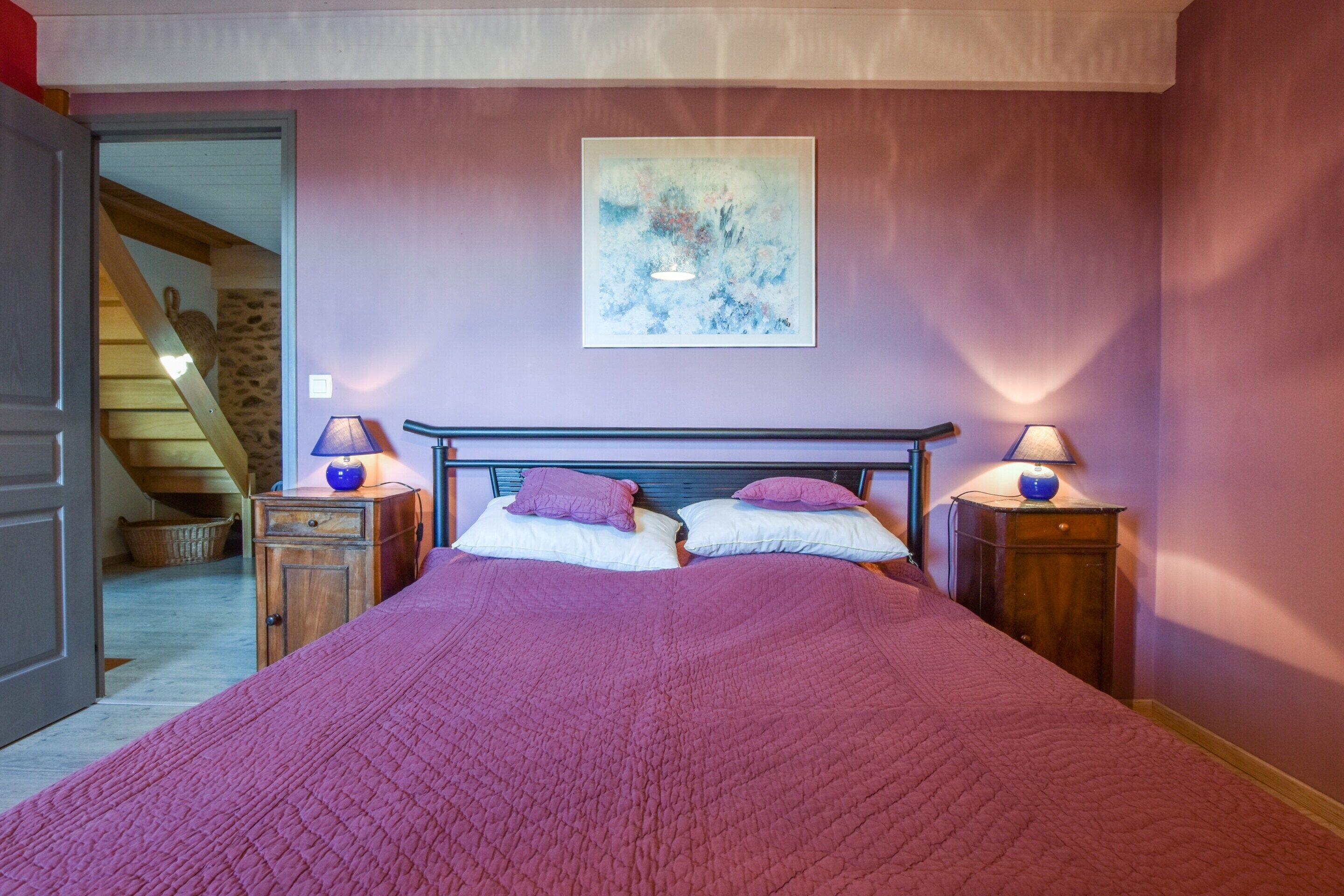 Een slaapkamer met een groot bed, twee bedlampjes en een schilderij aan de muur.