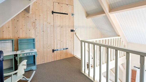 A loft-style room with a wooden slat wall, a kitchenette with a stove and sink, and a balcony with a white railing. - Holiday Home in Overberg With Garden and Terrace (Overberg)