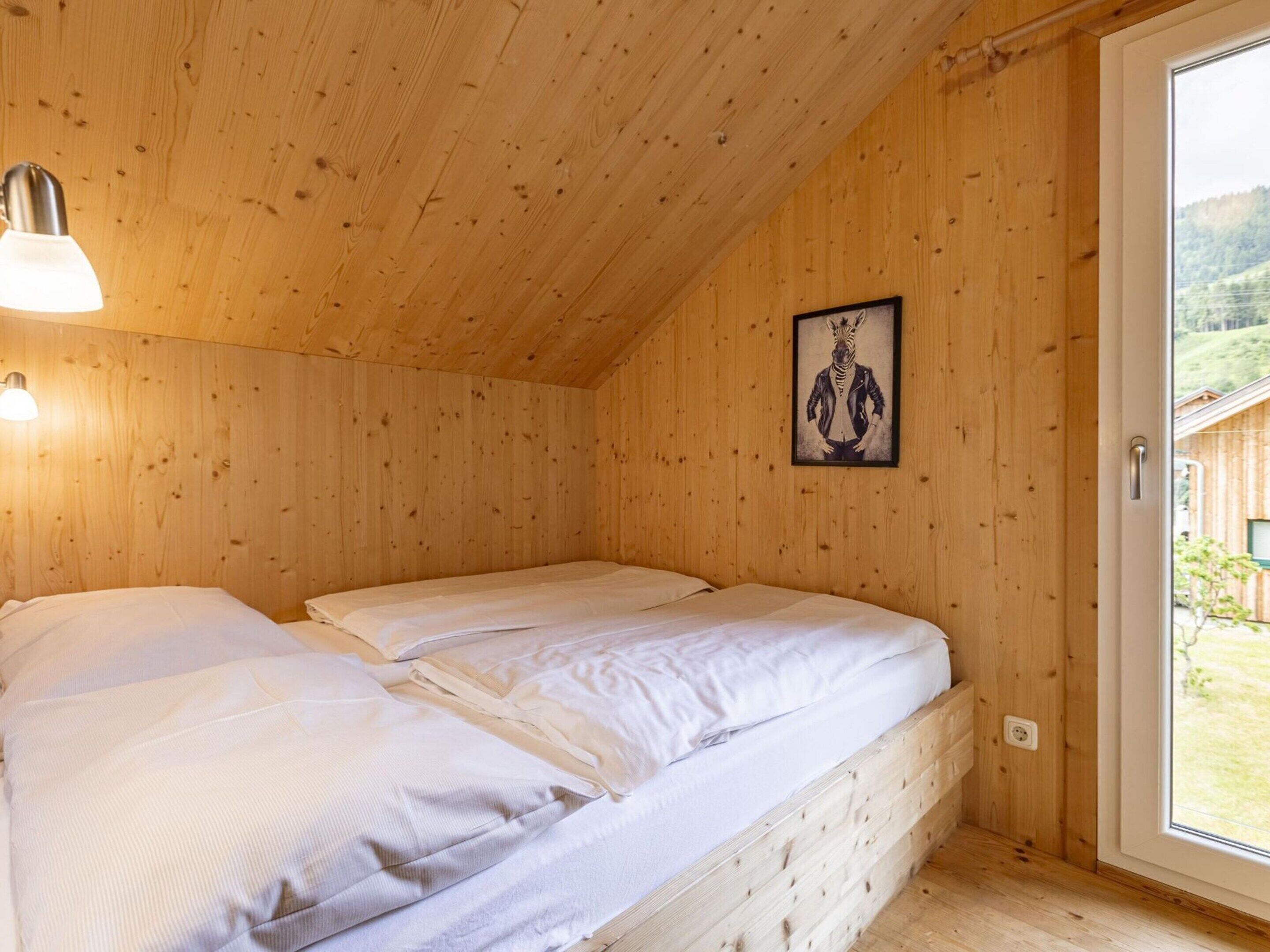 Una habitación de madera con una cama, un cuadro en la pared y una ventana.