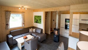 A modern cabin interior with a sofa, chairs, a table, a kitchen area, and a wood-burning stove. - Chalet With Whirlpool tub (Sankt Georgen am Kreischberg)