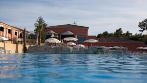 Une piscine avec un bâtiment en arrière-plan, agrémentée d’un espace extérieur avec des tables et des parasols.