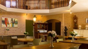 A dining area with brick walls, wooden tables, and chairs. There is a clock and a bookshelf in the background. - Luxury Mansion near Sea in Pingjum (Pingjum)