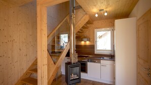 A wooden interior with a staircase, a kitchen area including a stove, and a window.