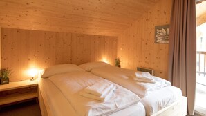 A wooden cabin bedroom with two beds, a nightstand, a lamp, and a window with curtains.