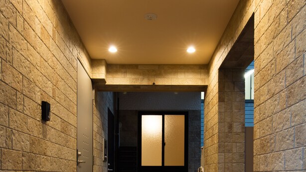 A hallway with stone walls and a tiled floor leading to a room with a sliding door. - Ginza Tsukiji GUEST HOUSE 301. (Chuo)