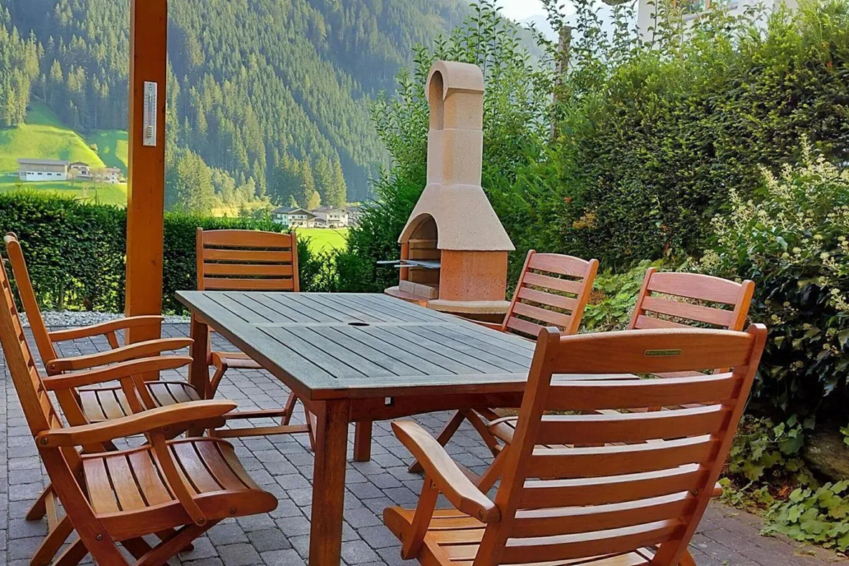 Un patio exterior con mesa y sillas, una parrilla de piedra y vistas a un paisaje montañoso.