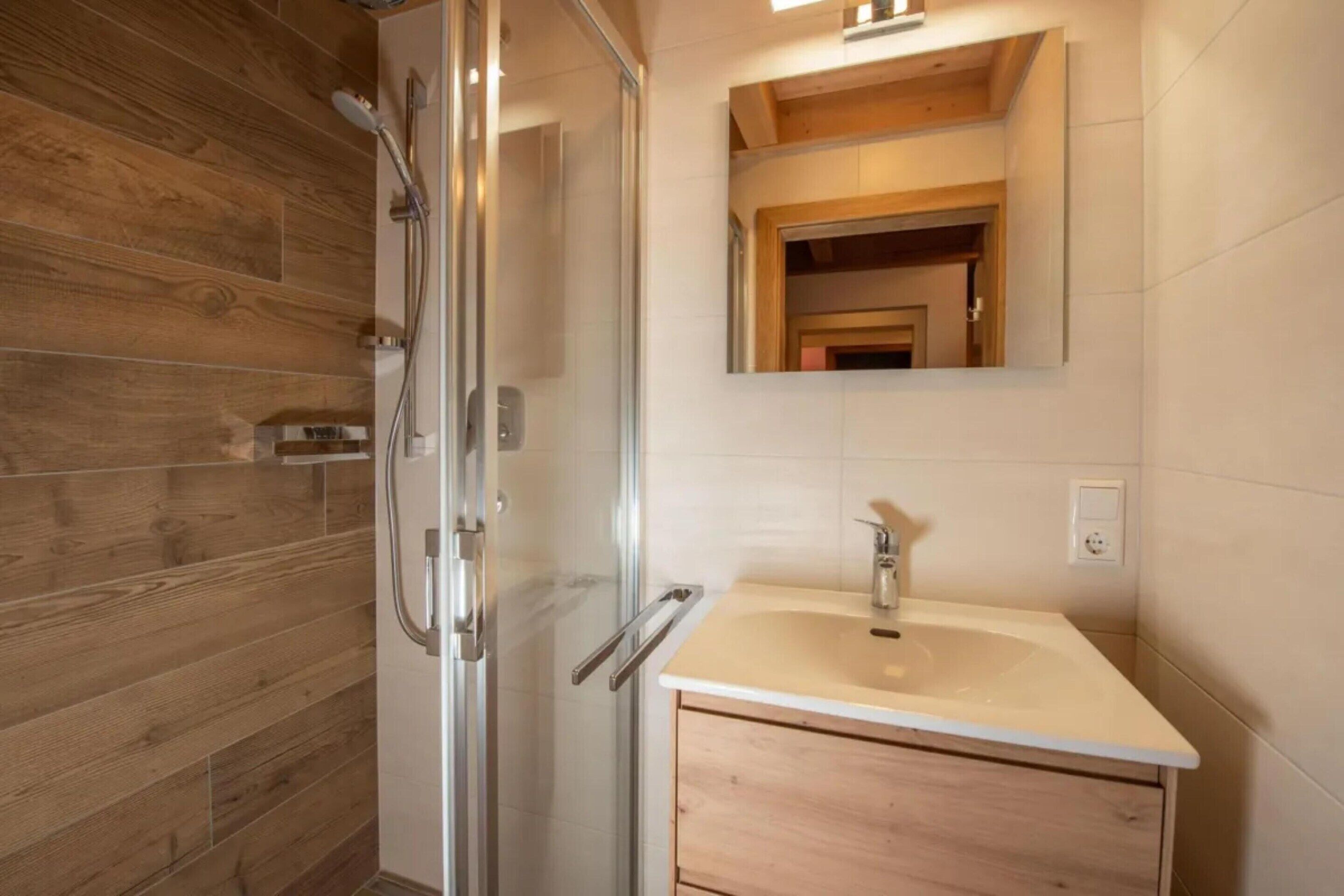Een moderne badkamer met een douchecabine van glas, een wastafel en een houten wastafelmeubel.