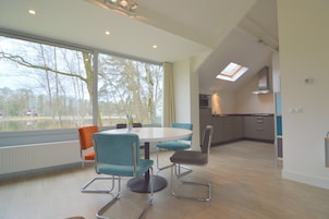 A modern kitchen with a skylight, a dining area with a round table and chairs, and a view of trees through large windows.