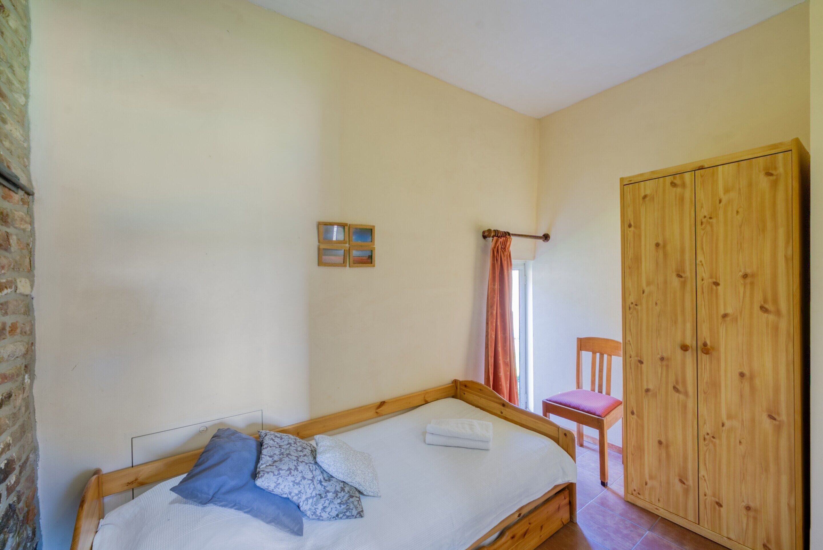 A bedroom with a wooden bed, a wooden wardrobe, and a small chair.
