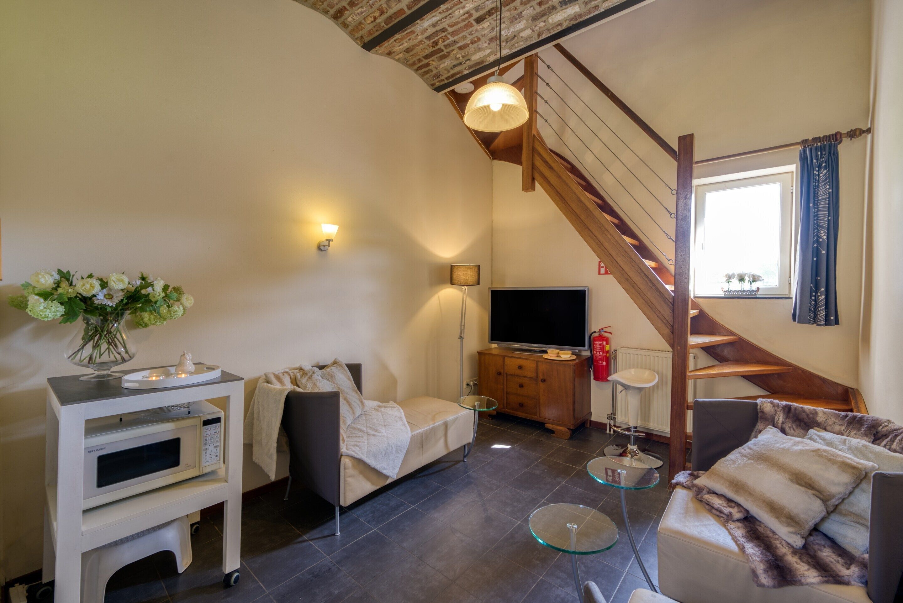 Una sala de estar acogedora con sofá, una mesa de centro, televisor, microondas y un mueble pequeño. Se ve una escalera que sube a un nivel superior.
