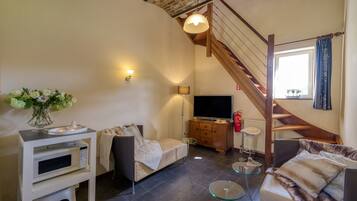 Una sala de estar acogedora con sofá, una mesa de centro, televisor, microondas y un mueble pequeño. Se ve una escalera que sube a un nivel superior.