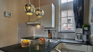 Una cocina con encimera negra, un cuenco de madera con limones, una estufa blanca y una ventana con vistas a edificios.
